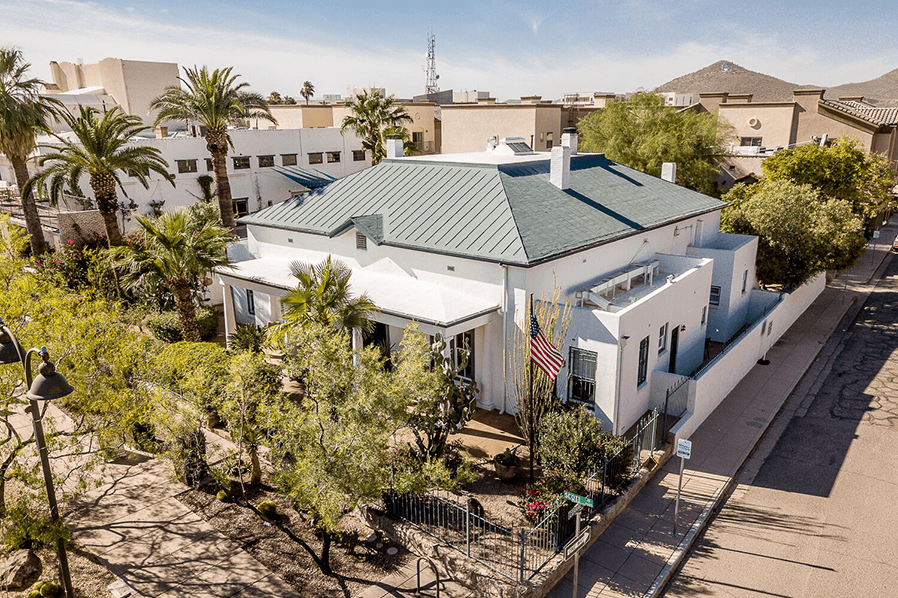 Aerial view of a white house with a green roof surrounded by palm trees and shrubs.